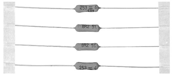 Vier zylindrische Widerstände mit langen Drahtanschlüssen sind horizontal ausgerichtet. Zwei sind mit '8R2 5%' und zwei mit '25R 1%' beschriftet.