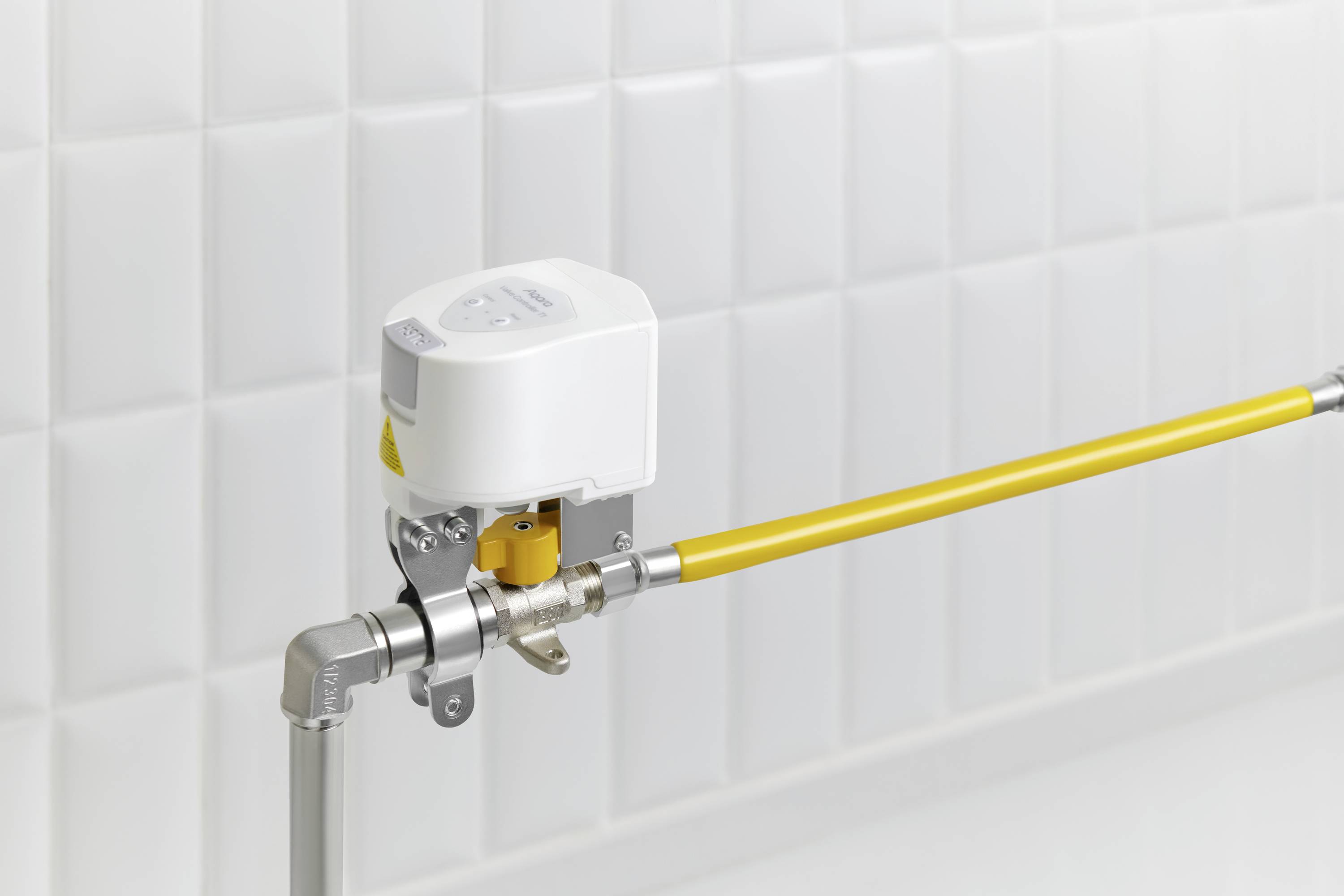 Ein elektrisches Ventil ist an einem gelben Rohr montiert, vor einer gefliesten weißen Wand, zeigt moderne Rohrleitungstechnik.