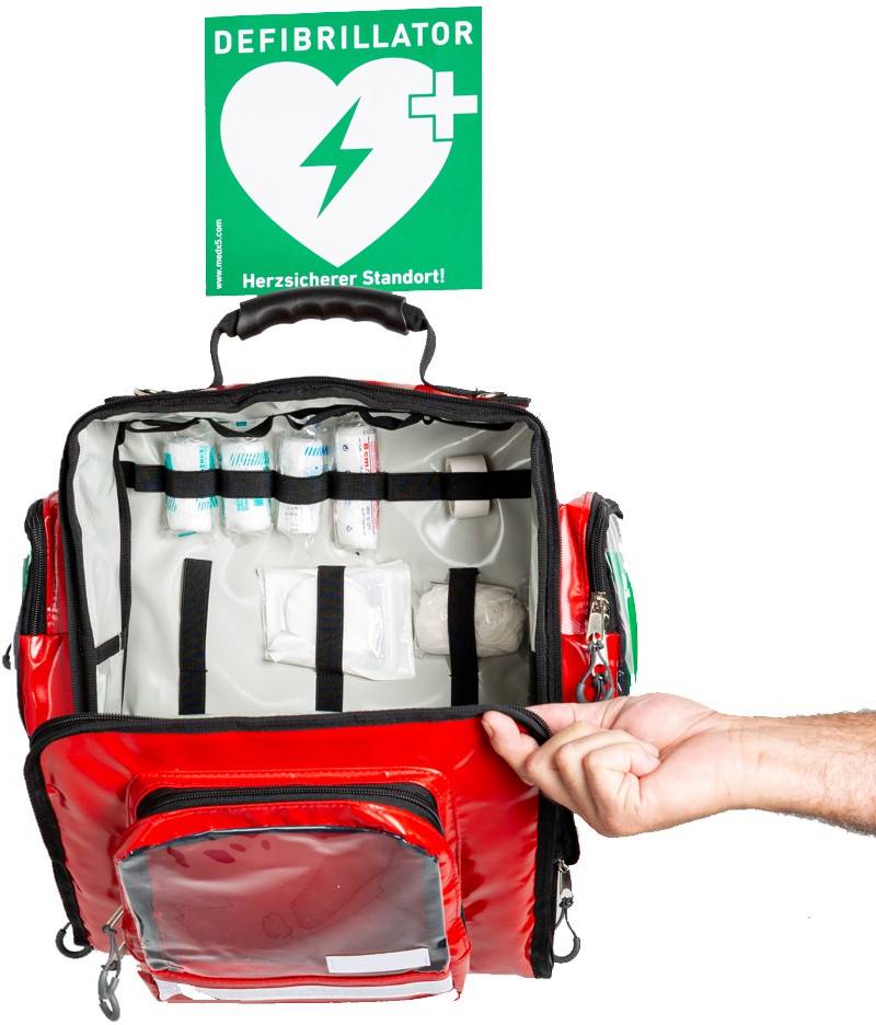 Ein roter Notfallrucksack mit Erste-Hilfe-Material wird geöffnet. Ein Schild zeigt 'Defibrillator' an einem sicheren Standort.