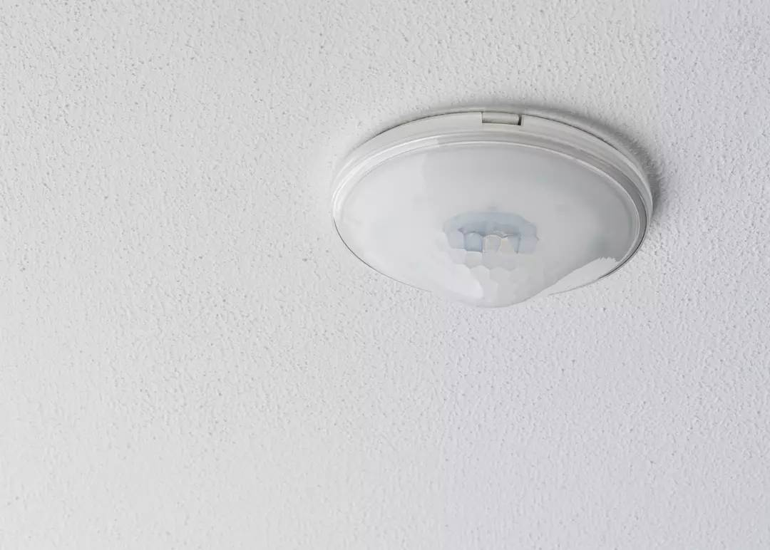 Deckenmontierter Bewegungsmelder in einem hellen Raum. Der Melder ist in einer runden, weißen Halterung an der Decke angebracht.