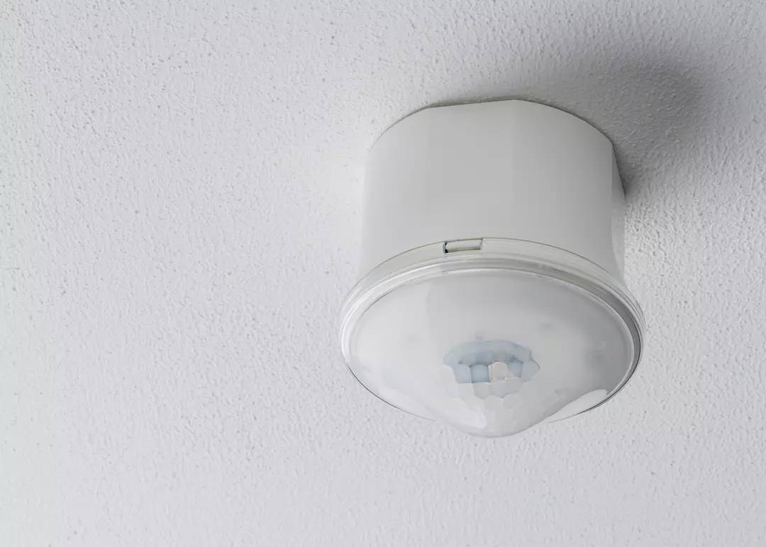 Ein runder Bewegungssensor ist an der weißen Decke montiert. Er dient zur Erkennung von Bewegungen im Raum.