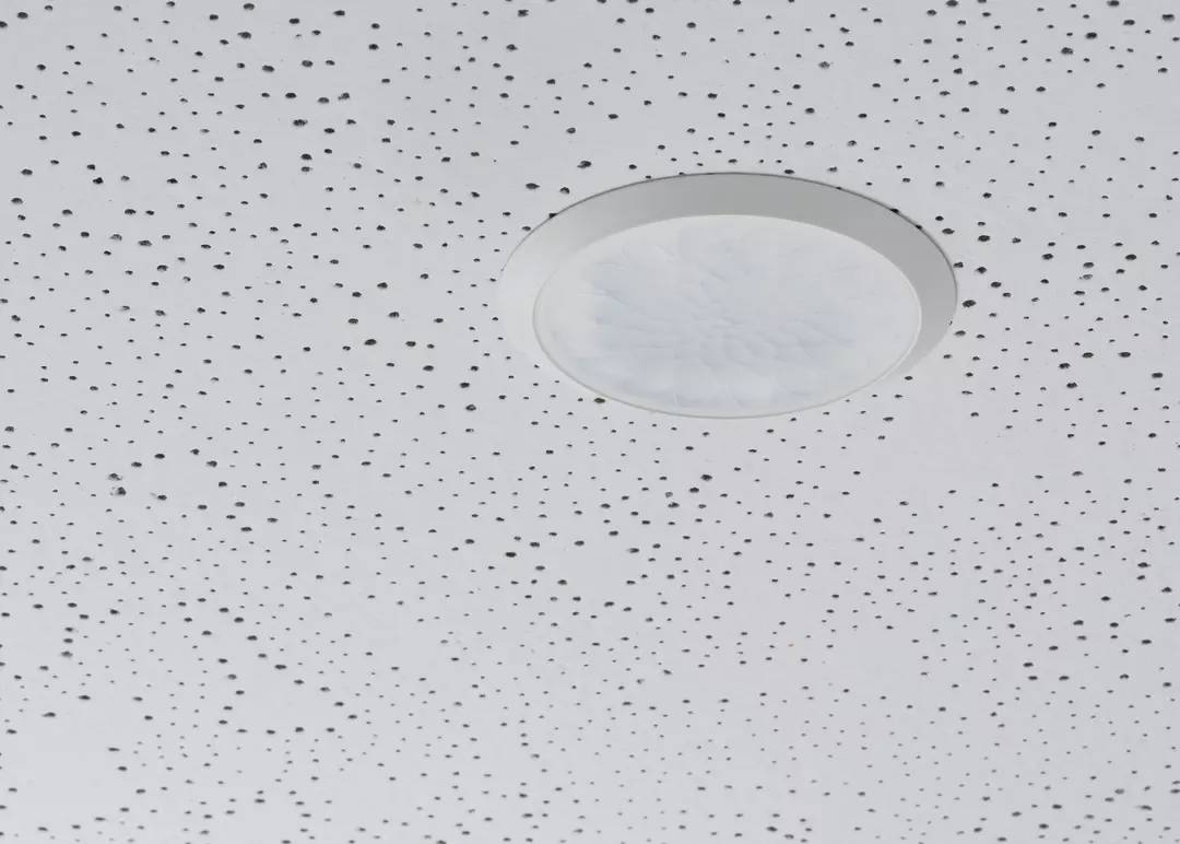 Eine weiße Decke mit unsymmetrischen schwarzen Punkten und einem runden, weißen Deckenlicht in der Mitte.