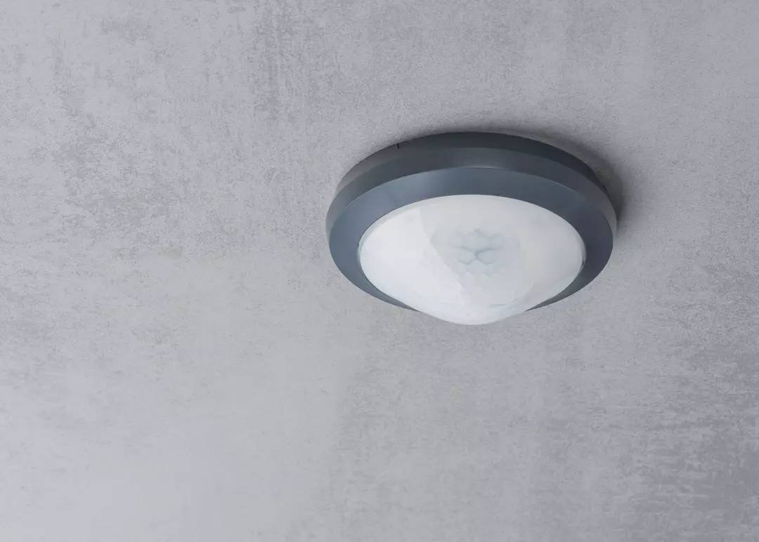 Deckenleuchte in modernem Design mit runder, weißer Abdeckung an grauer Decke.