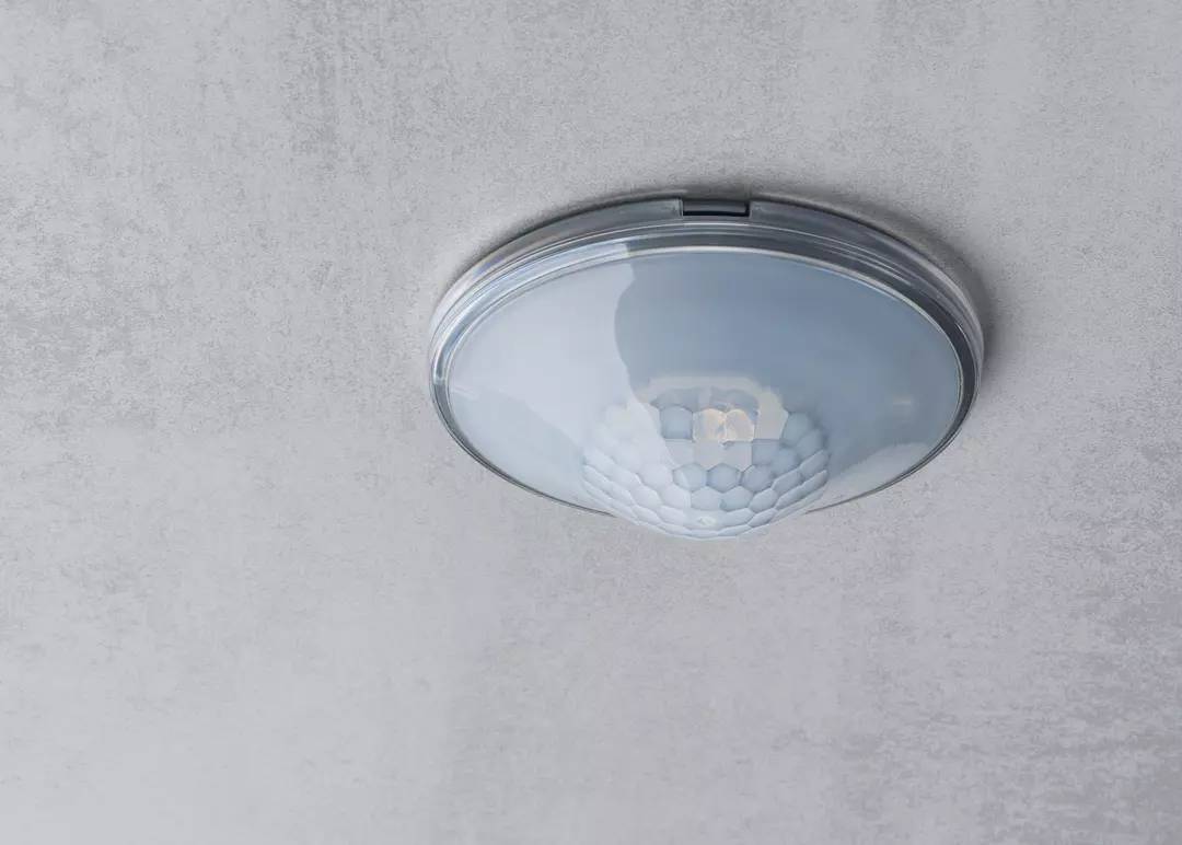 Ein Bewegungssensor an der Decke montiert. Der Sensor hat eine weiße Abdeckung und ist für die Erkennung von Bewegungen im Raum.