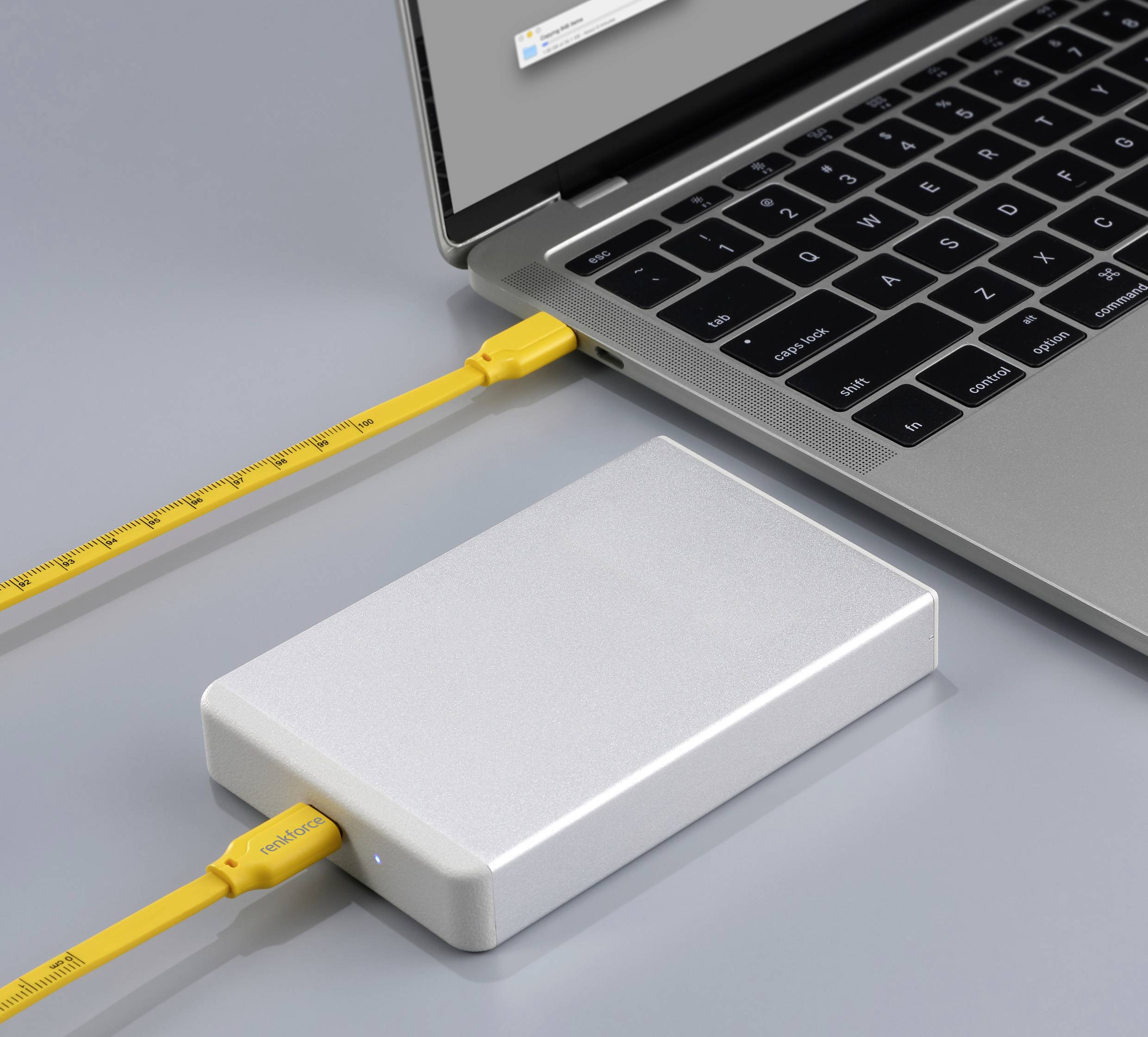 Externe Festplatte in Silber ist über ein gelbes USB-Kabel mit einem Laptop verbunden, der einen grauen Bildschirm zeigt.