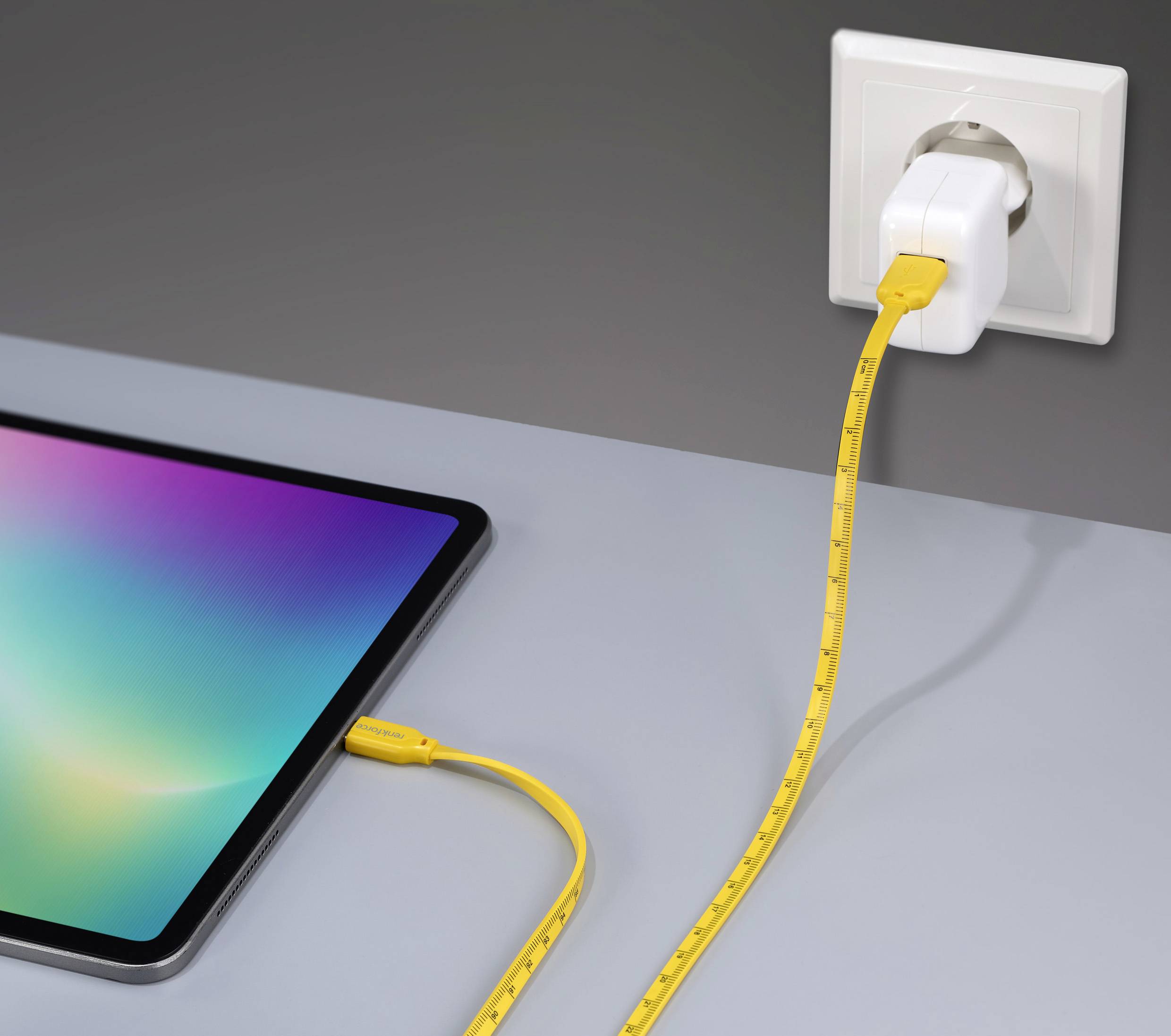 Tablet auf Tisch mit gelbem Ladekabel in Steckdose.