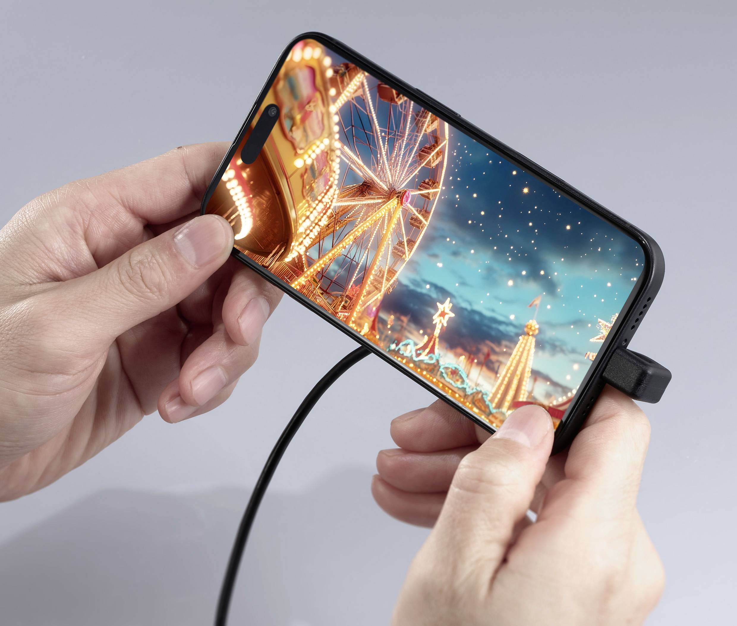 Person hält ein Smartphone in den Händen, auf dem ein leuchtendes Riesenrad in einem Vergnügungspark bei Nacht angezeigt wird.