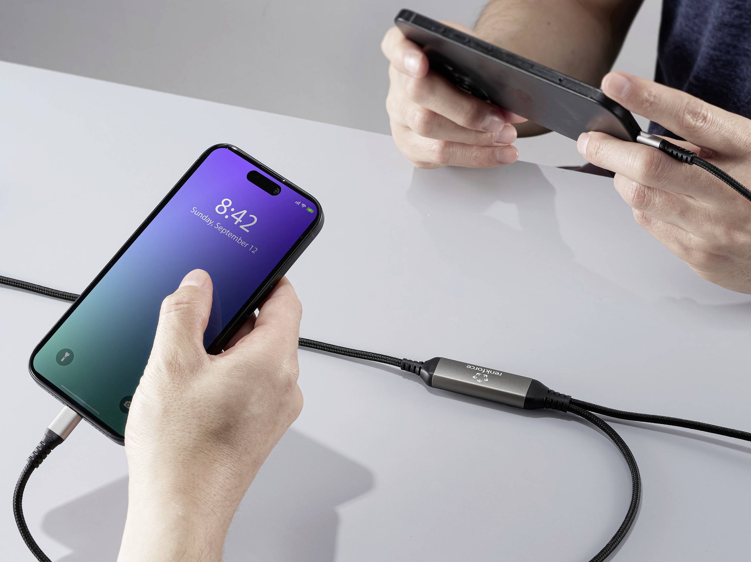 Zwei Personen verwenden miteinander verbundene digitale Geräte. Links zeigt ein Smartphone-Bildschirm die Uhrzeit 8:42 an.