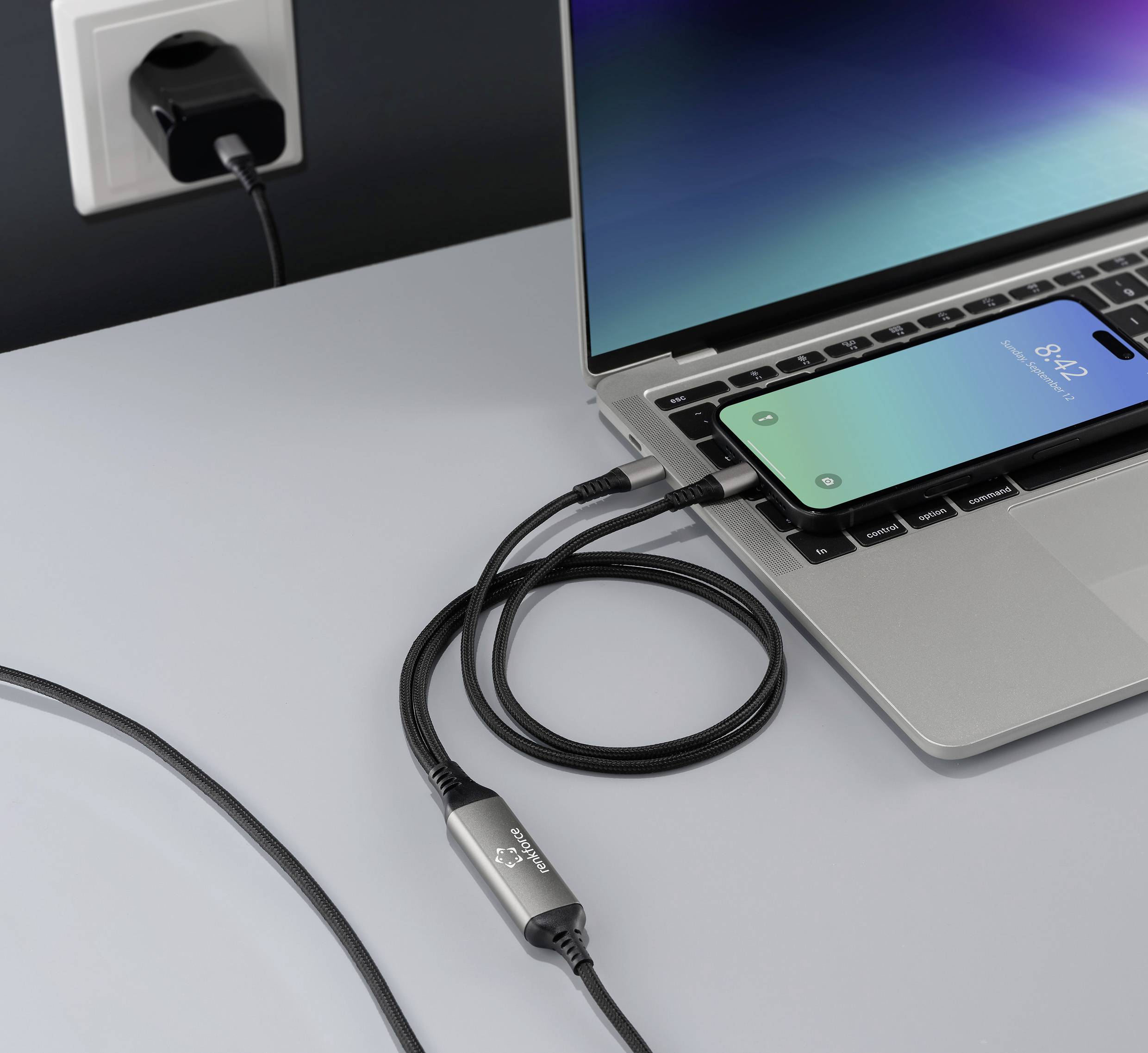 Ein Smartphone wird über ein USB-Kabel an einen Laptop angeschlossen, auf dem Tisch befindet sich eine Steckdose.