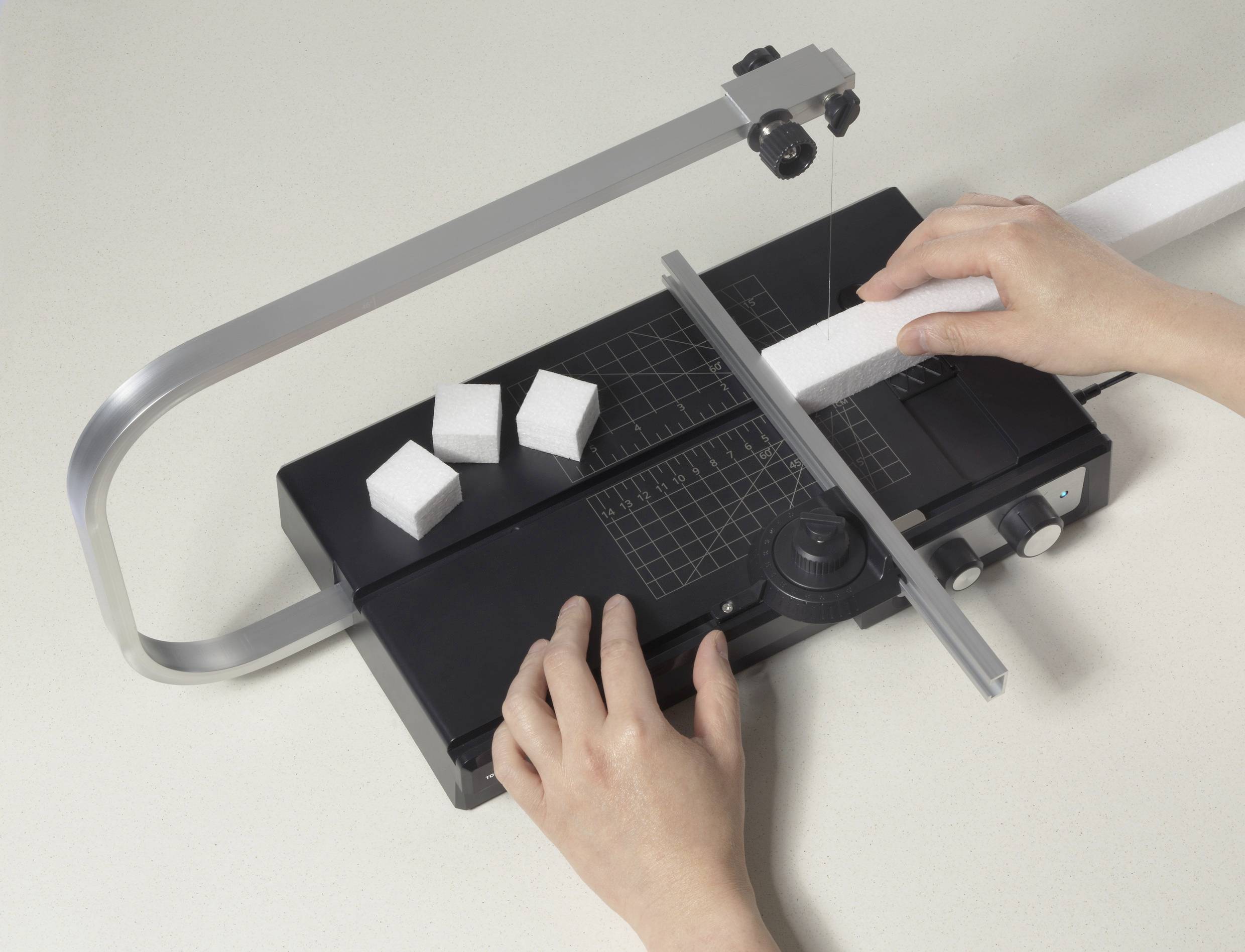 Eine Person schneidet Styroporblöcke mit einem heißen Drahtschneider. Drei abgeschnittene Blöcke liegen neben dem Gerät.