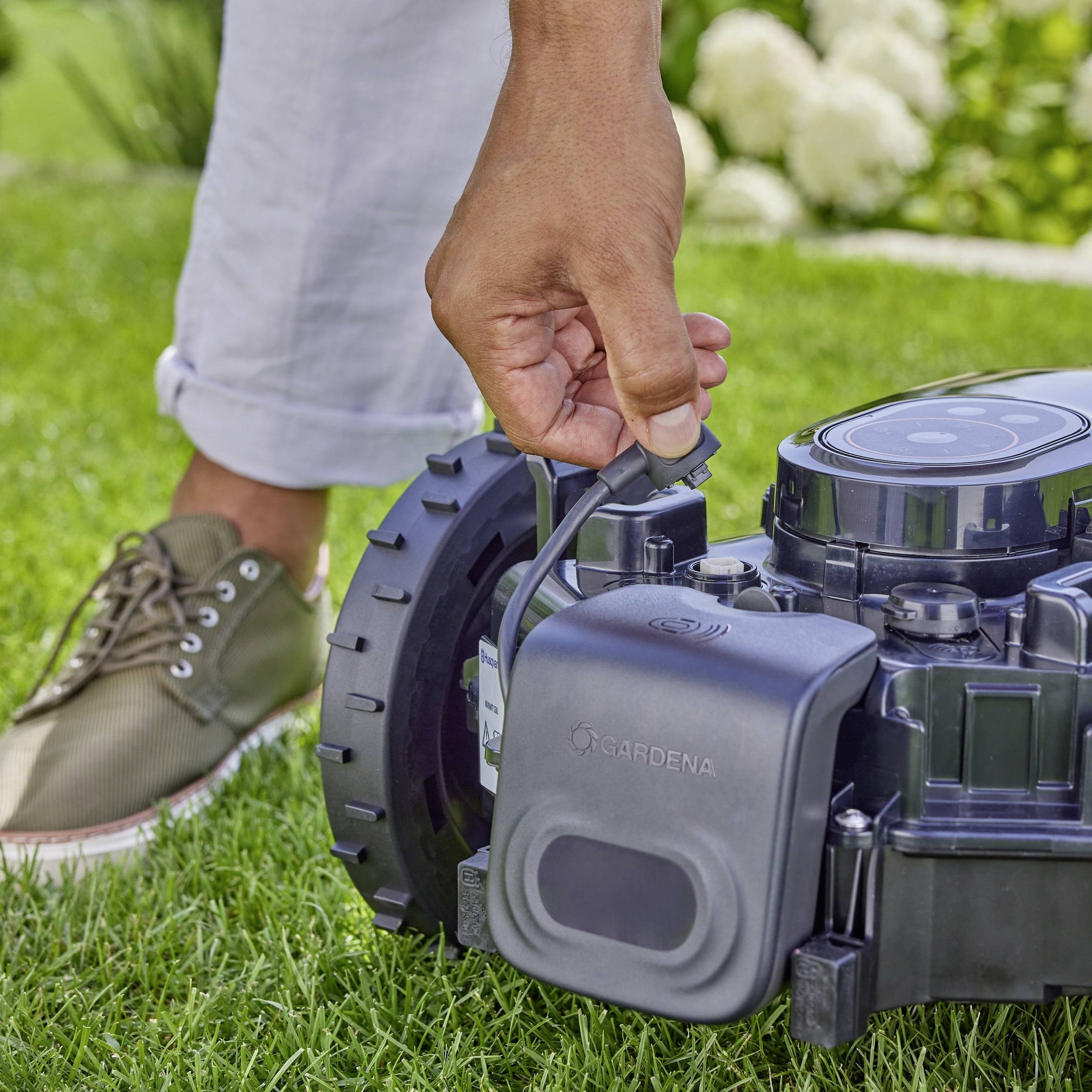Eine Person stellt die Höhe eines Rasenmähroboters auf einer grünen Wiese ein.