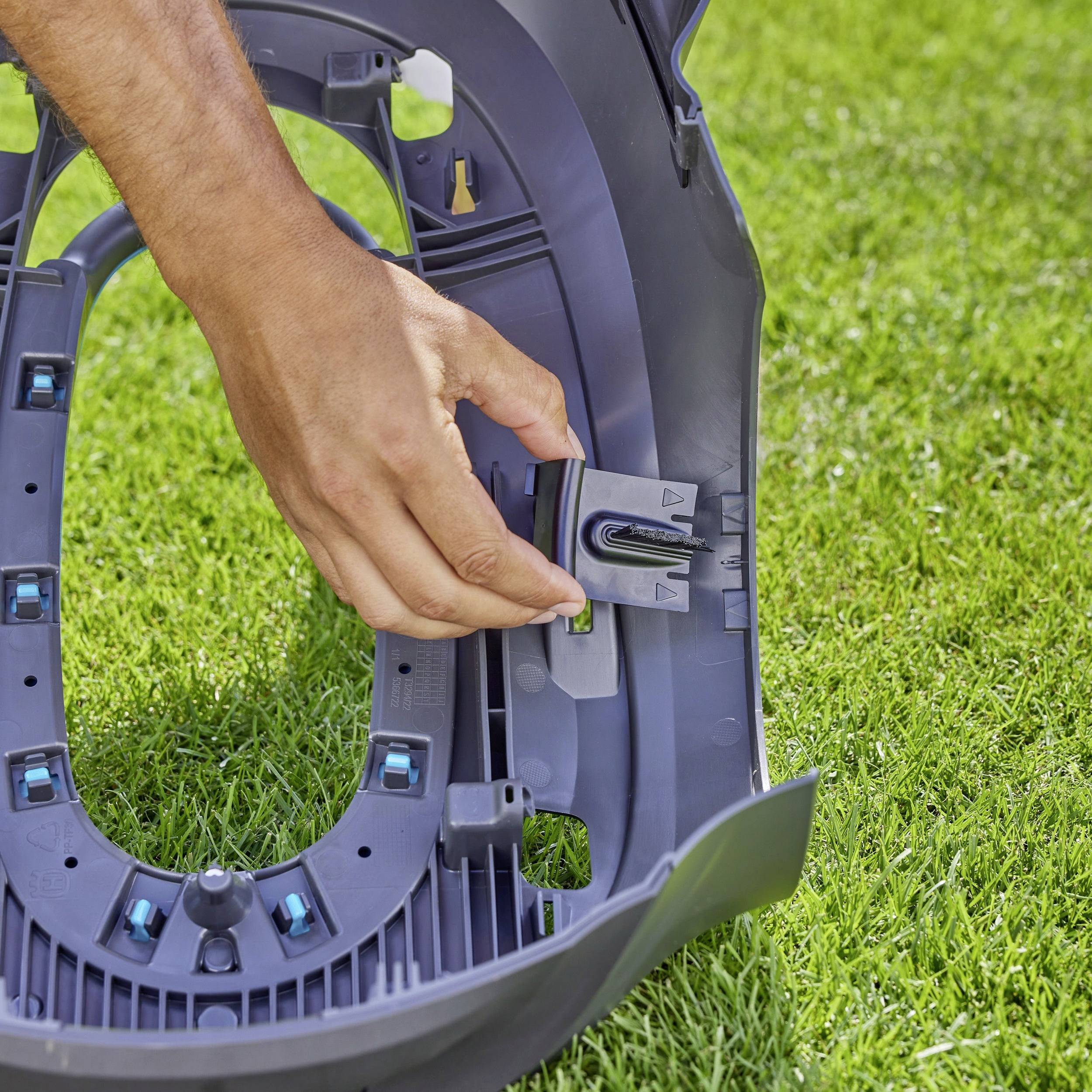 Eine Person montiert ein Ersatzteil auf einem Rasen. Konzentrierte Handarbeit an Plastikkomponenten, um eine Funktion zu reparieren oder anzupassen.