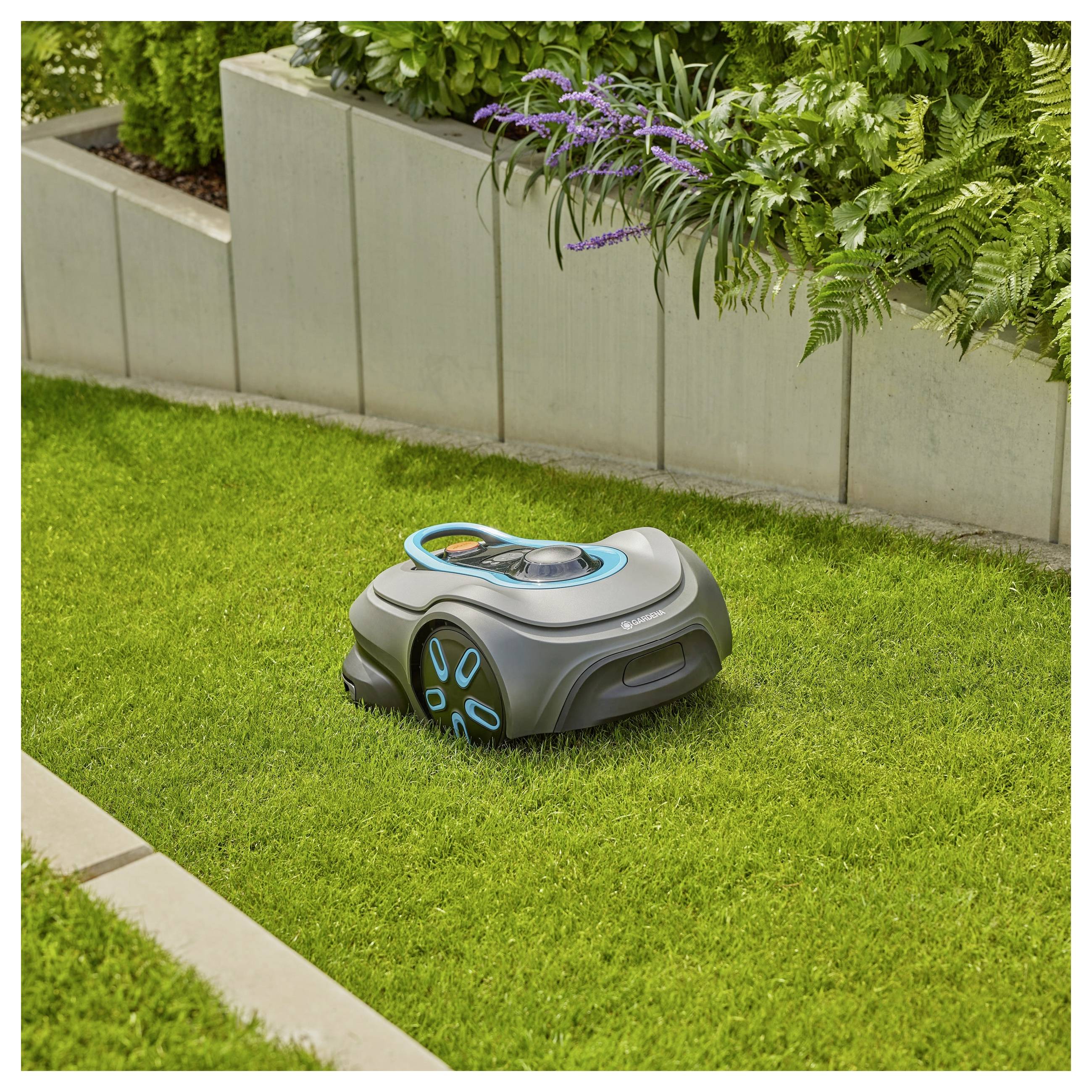 Ein Roboterrasenmäher mäht autonom einen kleinen Bereich des Grases in einem Garten, der von Betonkübeln und verschiedenen Pflanzen begrenzt wird.