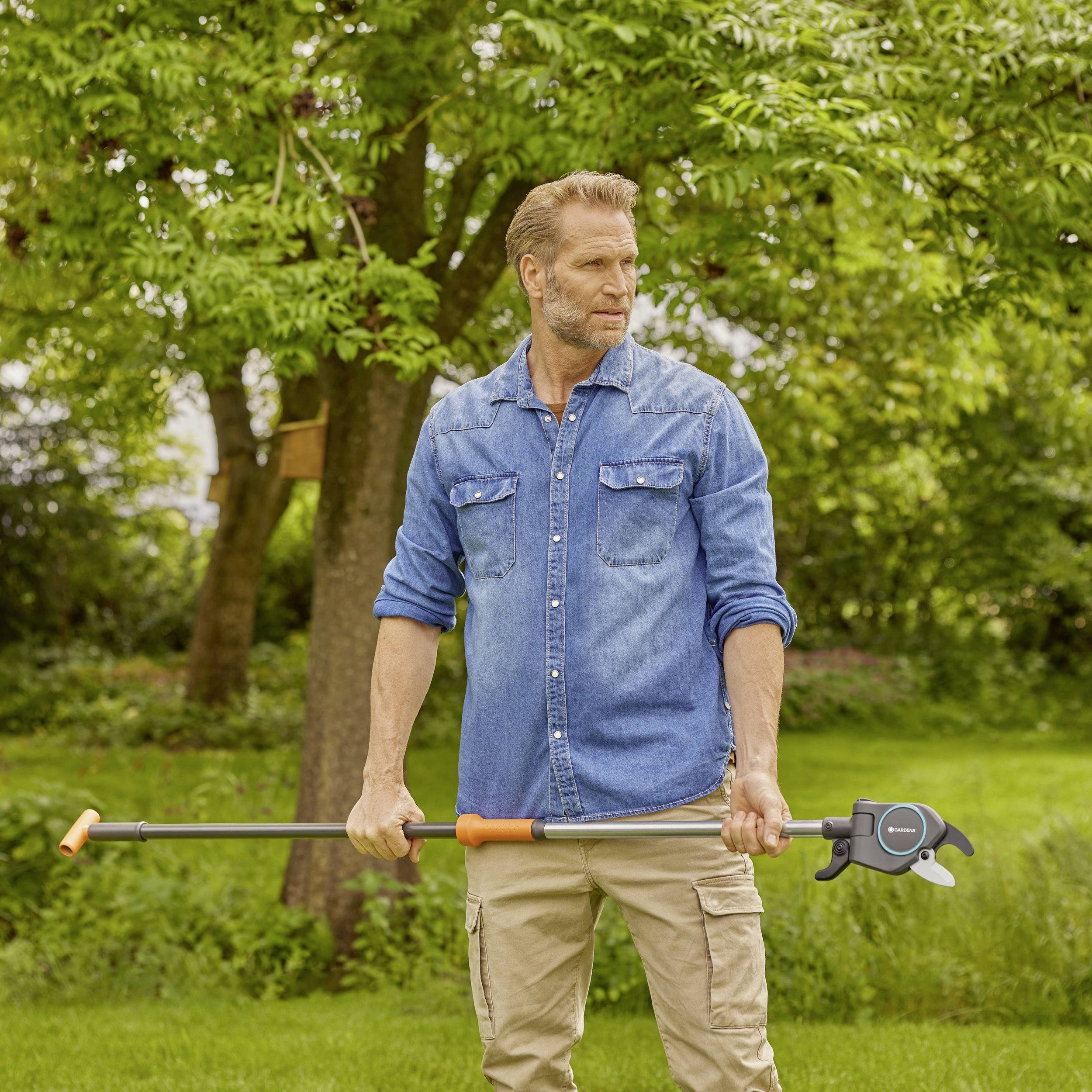 Ein Mann steht in einem Garten und hält einen Greifarm. Im Hintergrund sind grüne Bäume und Rasen zu sehen.