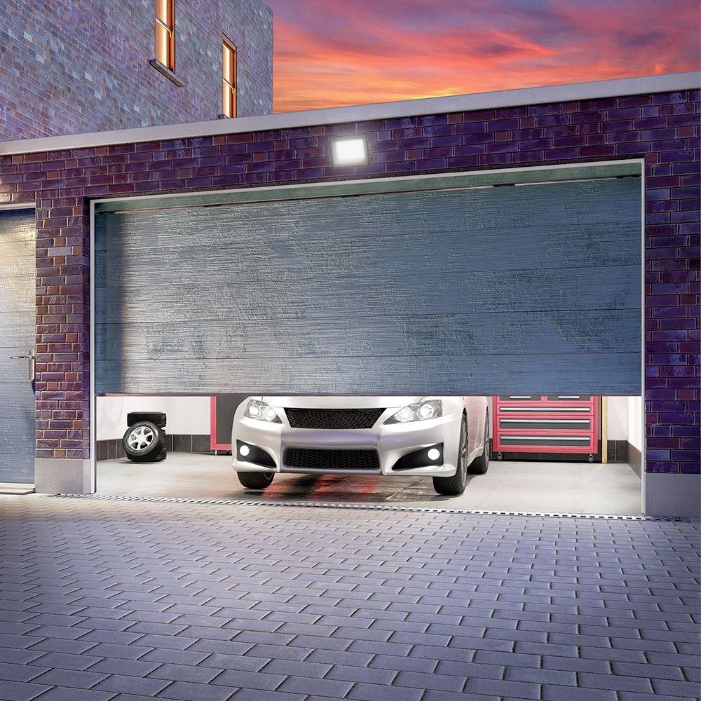 Ein weißes Auto fährt aus einer halb geöffneten Garage mit roten Wänden und Werkzeugkästen im Hintergrund bei Sonnenuntergang heraus.