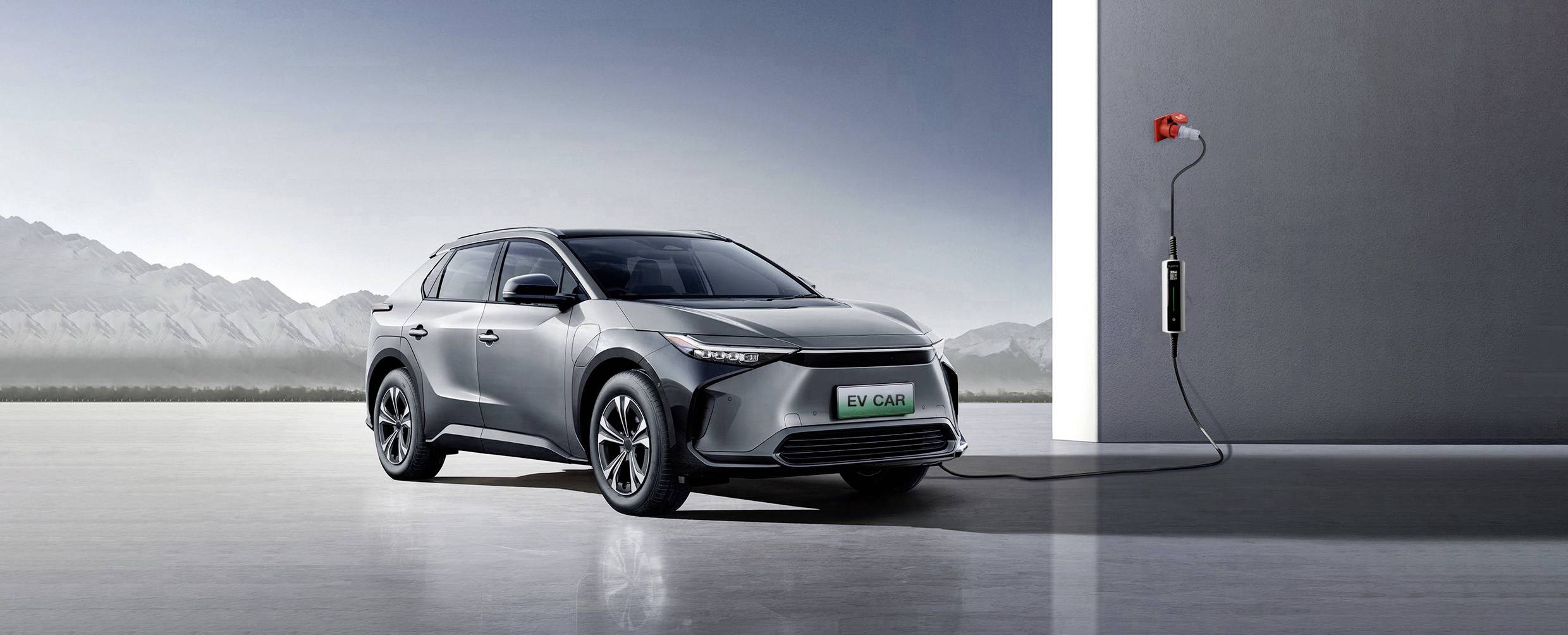 Ein silbernes Elektroauto wird an einer Ladestation aufgeladen. Im Hintergrund sind Berge und ein strahlend blauer Himmel zu sehen.