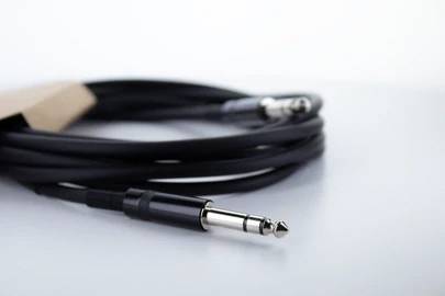 Ein schwarzes Audiokabel mit Klinkenstecker liegt auf einem Tisch. Der Fokus liegt auf dem glänzenden Stecker im Vordergrund.