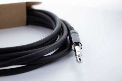 Schwarzes Audiokabel mit 3,5-mm-Klinkenstecker, teilweise aufgerollt, liegt auf einem weißen Hintergrund.