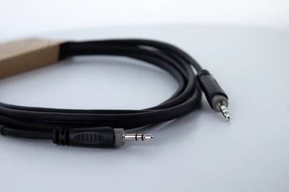Ein schwarzes Audiokabel mit einem 3,5-mm-Klinkenstecker an beiden Enden liegt auf einer weißen Oberfläche.