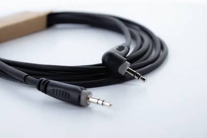 Schwarzes Audiokabel mit zwei 3,5-mm-Klinkensteckern, aufgerollt auf einem weißen Hintergrund liegend.