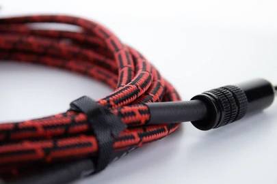 Ein rot-schwarz gemustertes Audiokabel mit einem Stecker, zusammengerollt und von einem Klettband zusammengehalten.