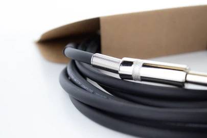 Nahaufnahme eines zusammengerollten Audiokabels mit Metallstecker, das teilweise aus einer braunen Verpackung herausragt.