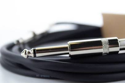 Ein schwarzes Audiokabel mit einem silbernen Klinkenstecker liegt aufgerollt auf einem Tisch.
