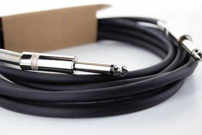 Schwarzes Audiokabel mit zwei silbernen Klinkensteckern, aufgerollt und auf weißem Untergrund liegend, für Musikinstrumente oder Audioequipment.