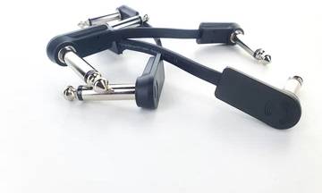 Zwei schwarze Gitarrenkabeladapter mit Metallsteckern liegen nebeneinander auf einem weißen Hintergrund.