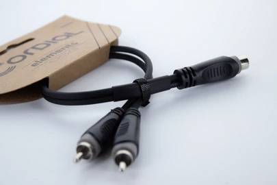 Ein schwarzes Audiokabel mit einem Adapter, präsentiert auf einer blauen Oberfläche. Links ist ein brauner Pappschuber erkennbar.