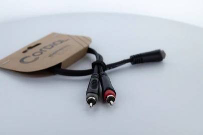 Ein Audiokabel mit zwei Cinch-Steckern und einem Klinkenstecker, befestigt an einem Pappetikett mit der Aufschrift 'Cordial'.