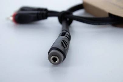 Ein schwarzes Audiokabel mit einem 3,5-mm-Stecker liegt auf einem weißen Untergrund und ist teilweise in eine Pappverpackung gesteckt.