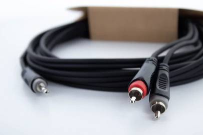 Schwarzes Audiokabel mit roten und weißen RCA-Steckern, aus einer braunen Kartonschachtel herausgeführt.