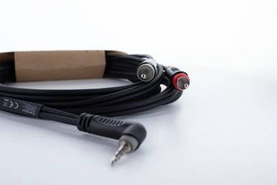 Ein schwarzes Audiokabel mit einem 3,5-mm-Stecker und zwei Cinch-Anschlüssen, einem roten und einem weißen, liegt auf einem Tisch.
