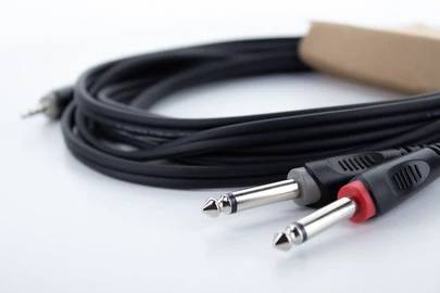 Zwei Audiokabel mit Klinkensteckern, eines schwarz, das andere mit rotem Ring, liegen aufgerollt auf einem weißen Tisch.