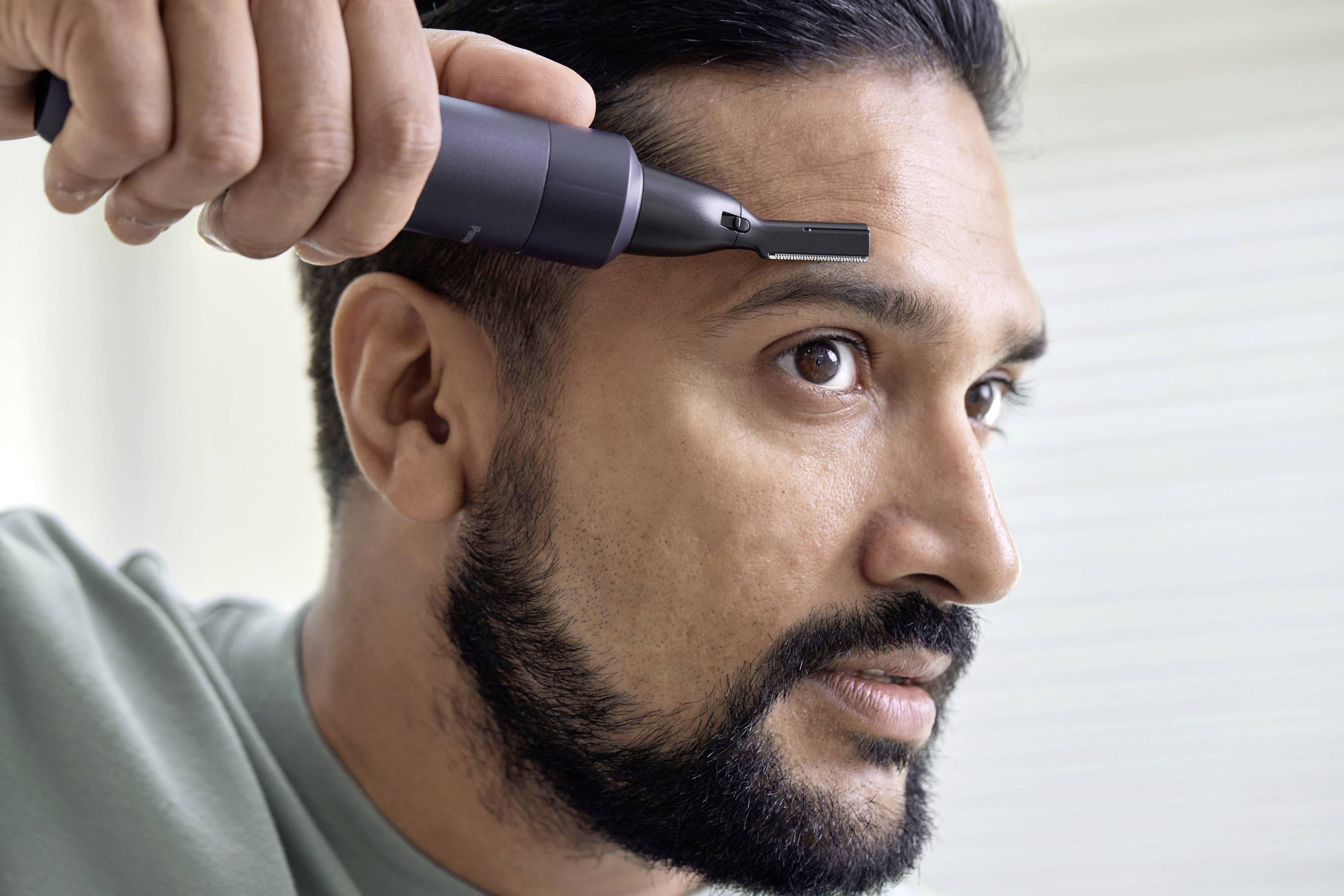 Ein Mann benutzt einen elektrischen Trimmer, um seinen Bart zu pflegen. Er konzentriert sich sorgfältig auf die Seite seines Gesichts.