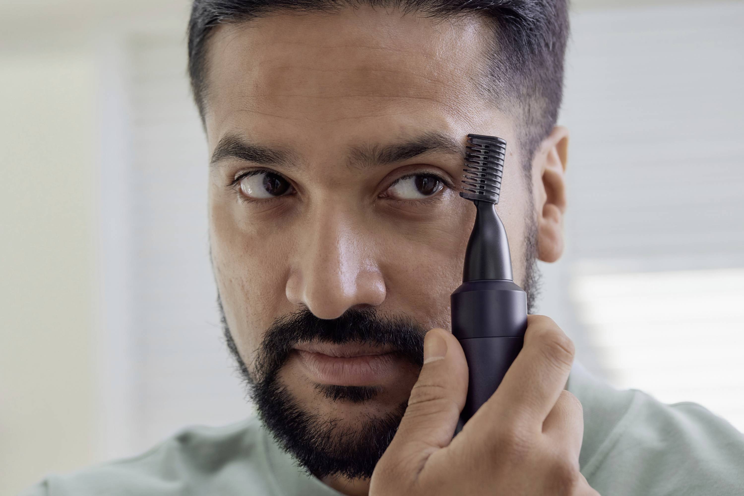 Ein Mann benutzt ein elektrisches Gerät, um seine Augenbrauen zu trimmen. Er konzentriert sich auf das präzise Stylen.