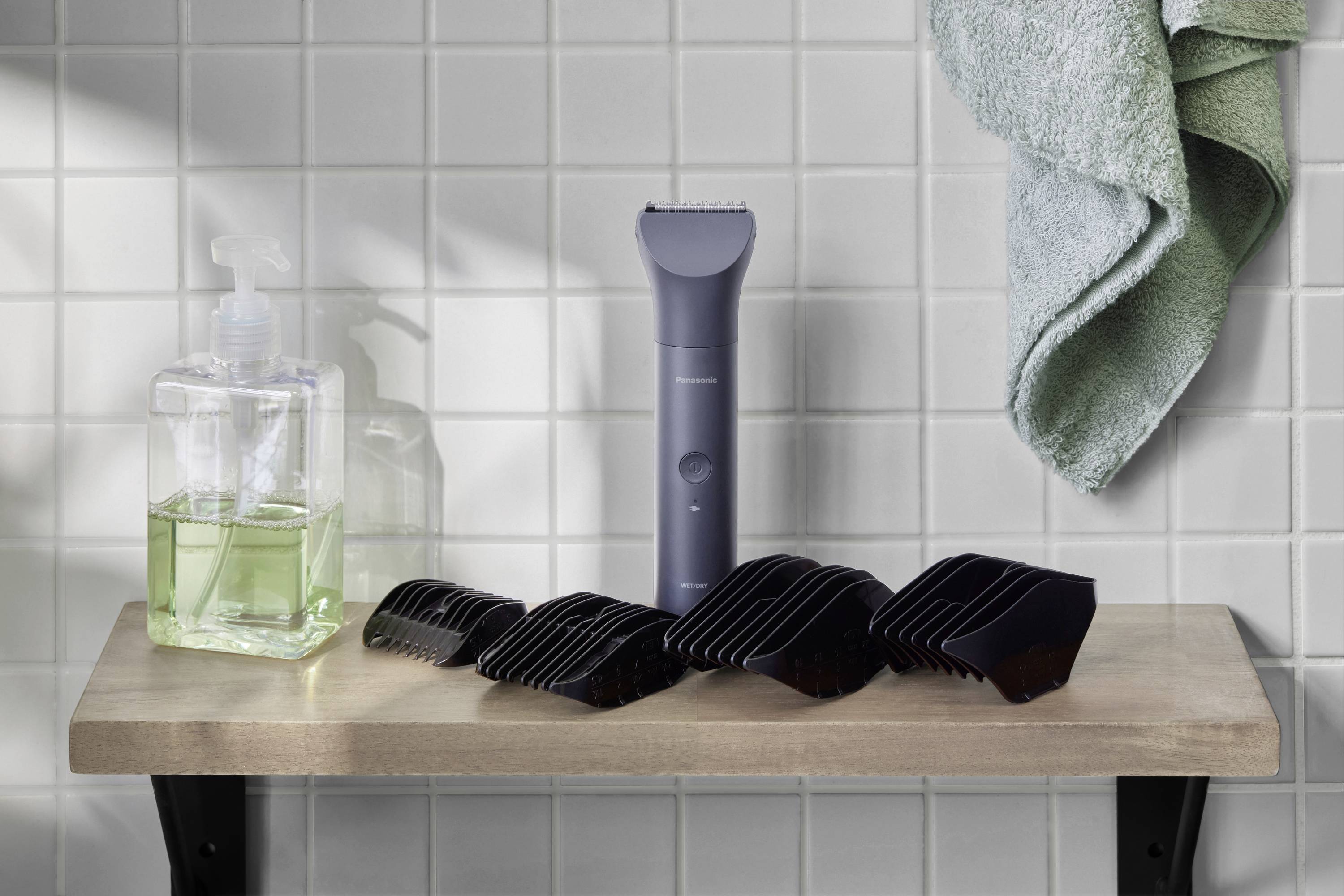 Rasierer und schwarze Aufsätze auf einem Regal im Badezimmer, neben einer Flüssigseife und einem grünen Handtuch.