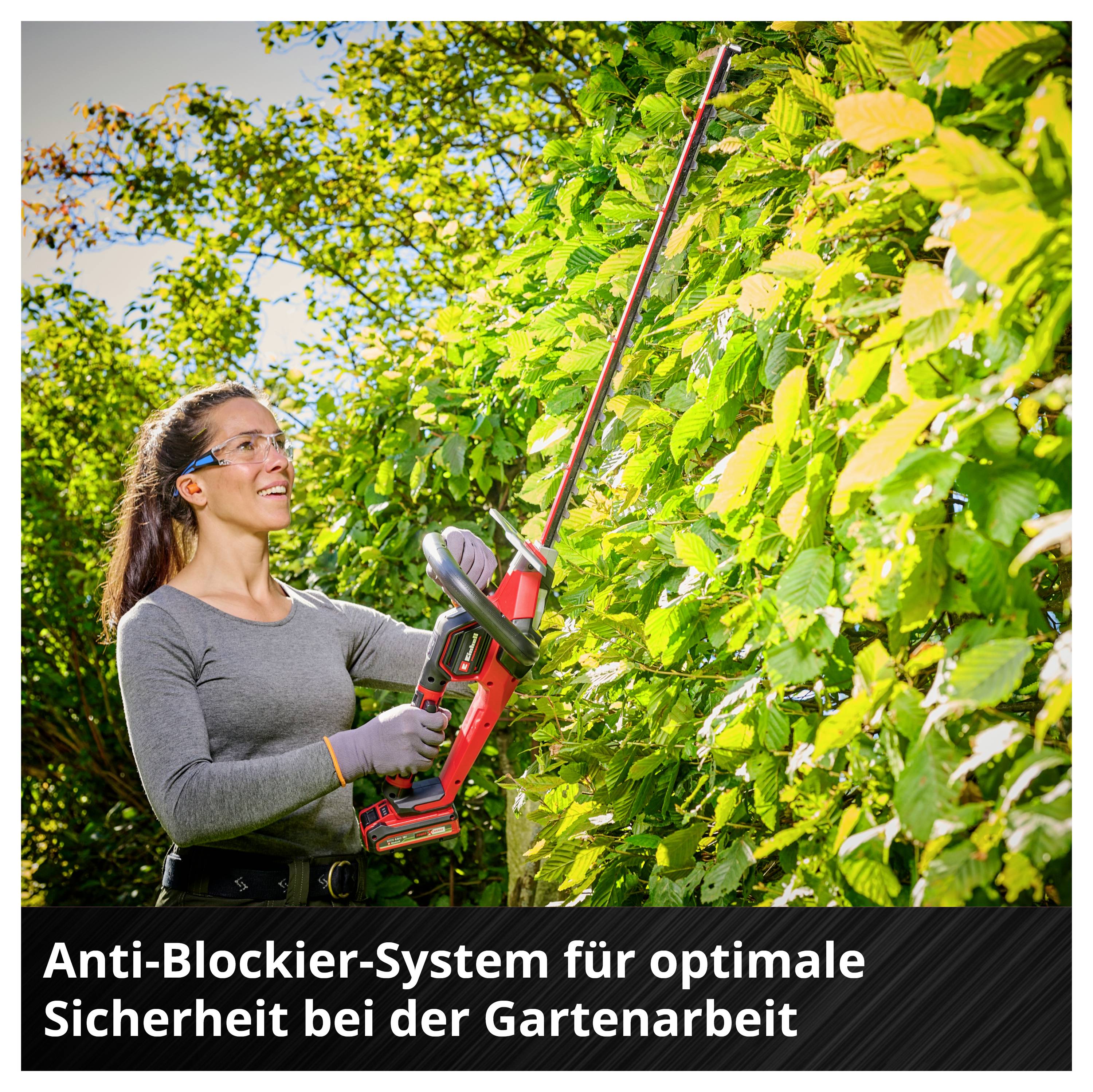 Frau nutzt eine Akku-Heckenschere zum Schneiden dichter Hecken; unten steht: 'Anti-Blockier-System für optimale Sicherheit bei der Gartenarbeit'