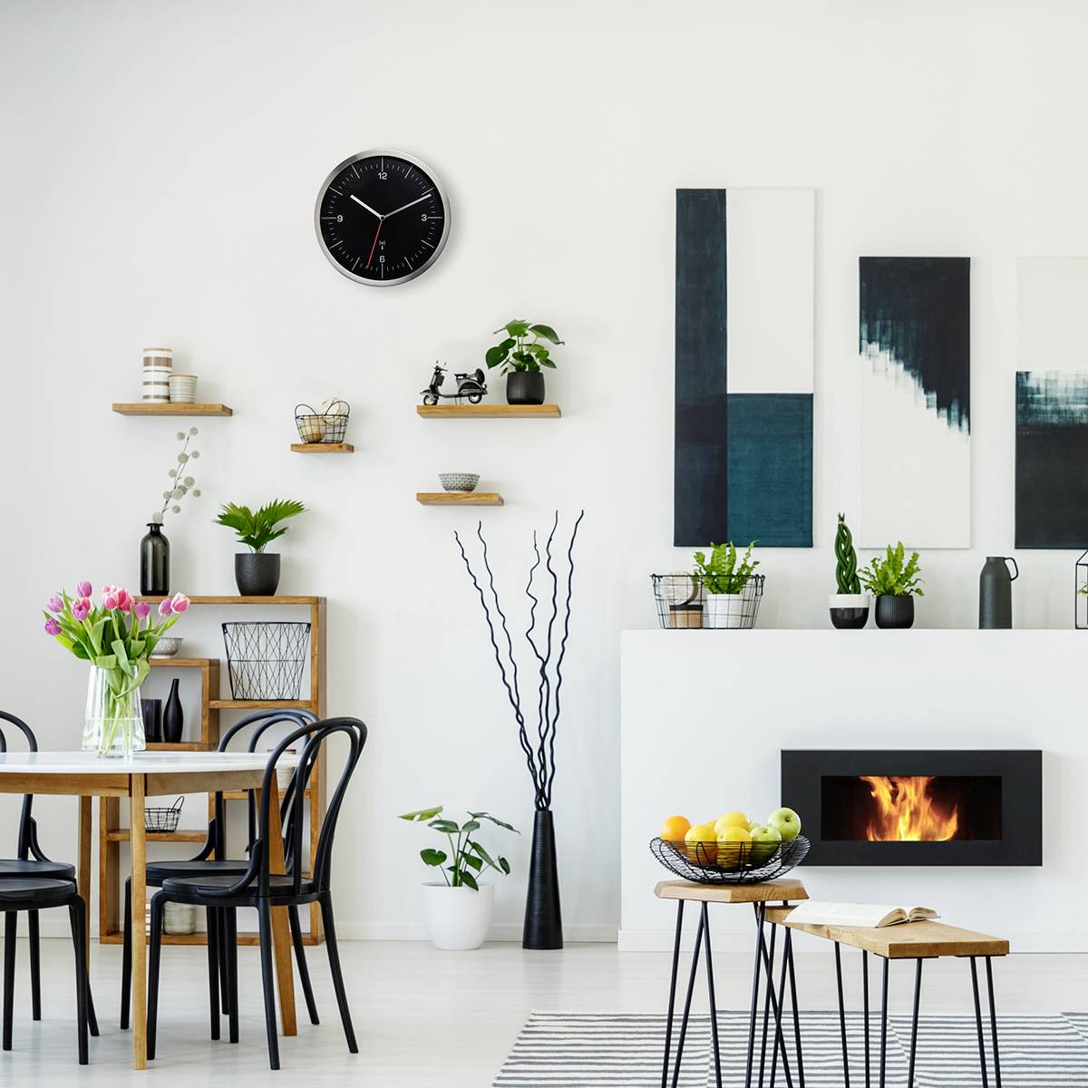 Esszimmer mit Tisch, vier Stühlen, Kamin, Regalen, Uhr und moderner Kunst an der Wand. Frische Blumen und Früchte dekorieren den Raum.