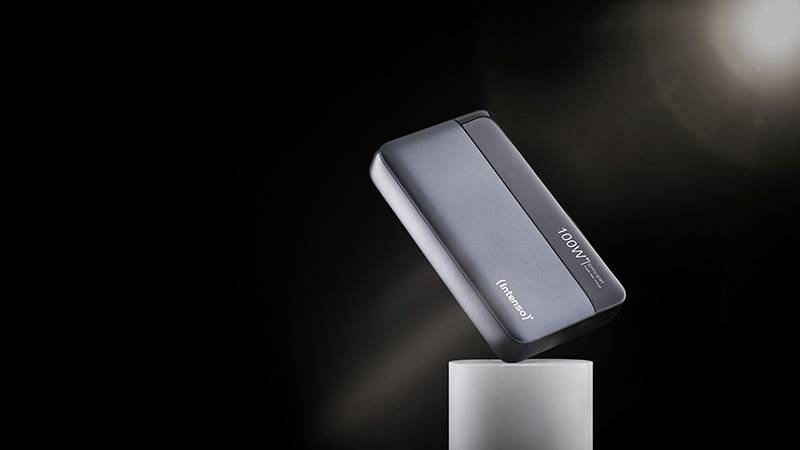 Eine schwarze, tragbare Powerbank schwebt leicht geneigt über einem zylinderförmigen Sockel vor einem schwarzen Hintergrund.