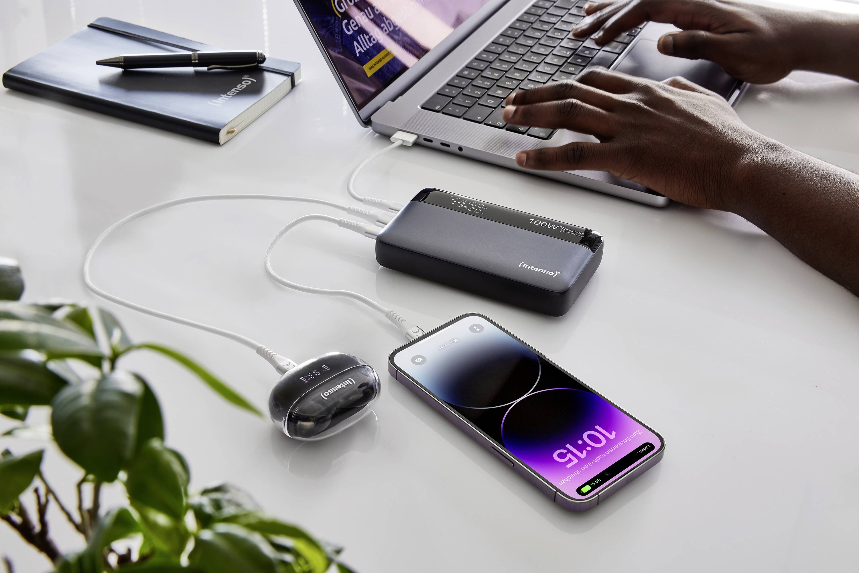 Eine Person arbeitet an einem Laptop, während ein Smartphone und ein anderes Gerät über eine Powerbank aufgeladen werden.