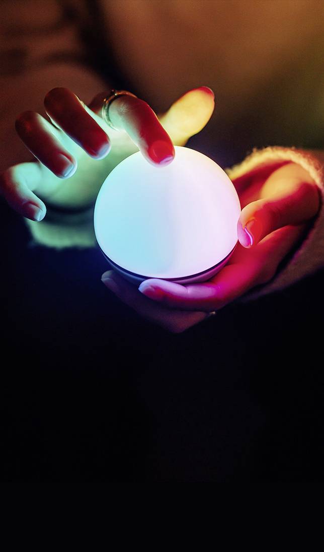 Zwei Hände halten eine leuchtende Kugel, die in verschiedenen Farben schimmert und eine warme Atmosphäre erzeugt.