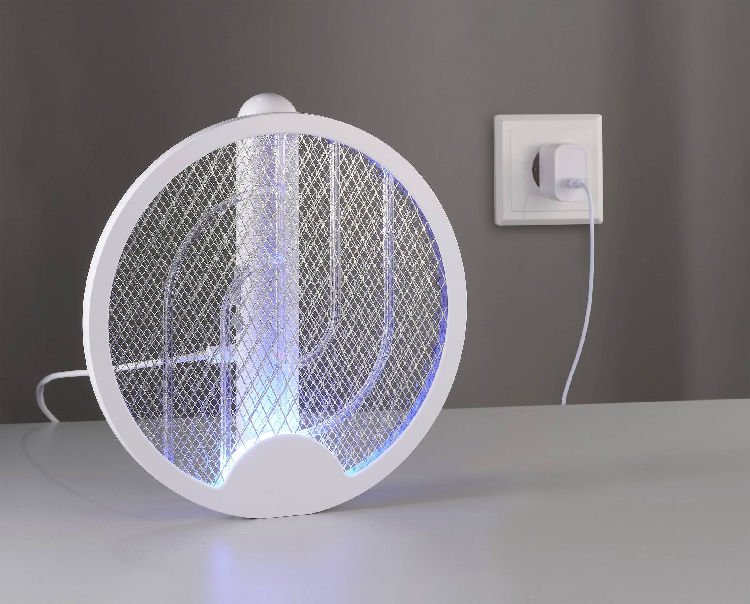 Ein elektrischer Insektenvernichter mit blauem Licht steht auf einem Tisch und ist über ein Kabel an eine Steckdose angeschlossen.