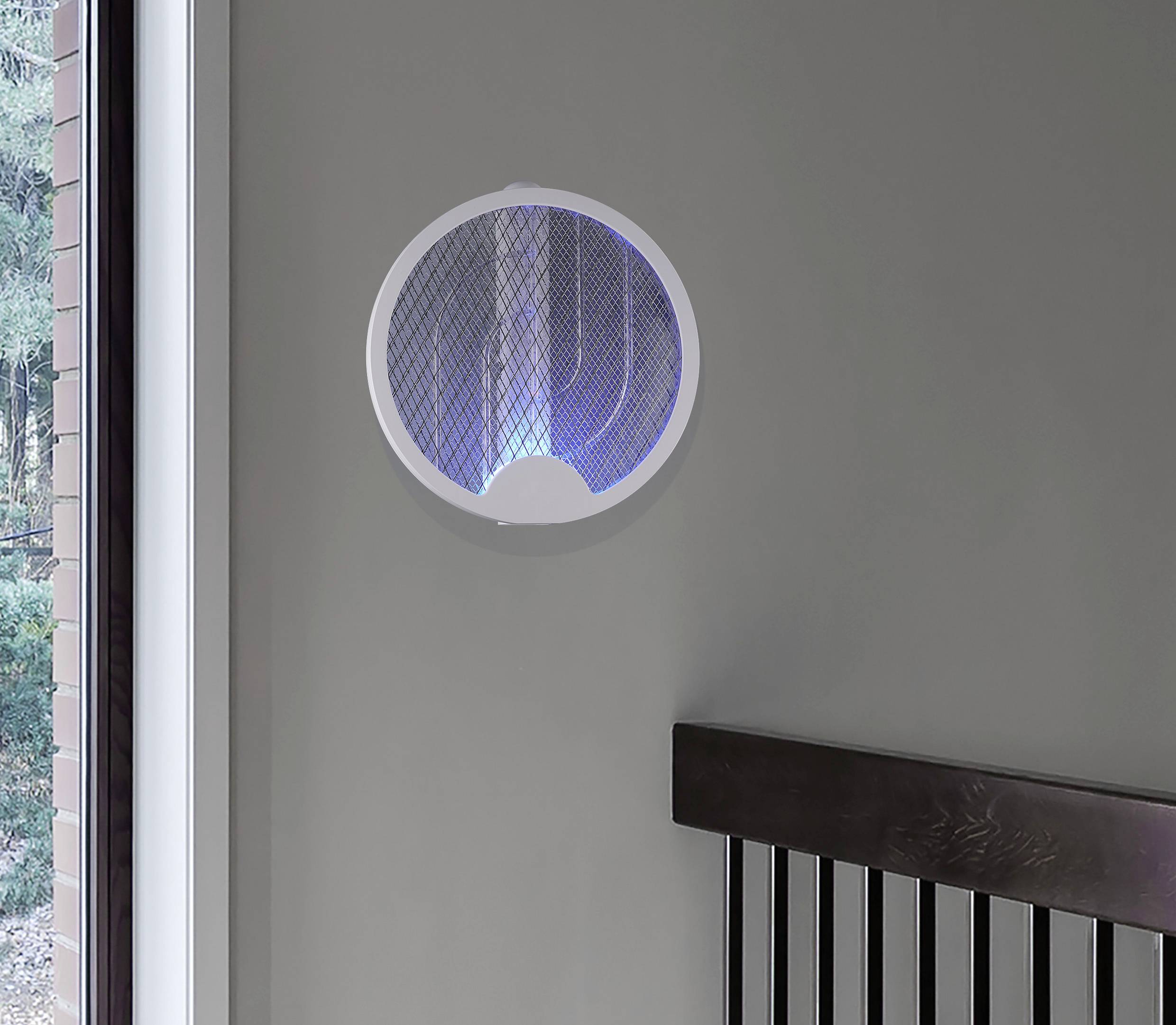 Eine runde, moderne Lampe mit blauem Licht hängt an einer grauen Wand. Links befindet sich ein Fenster mit Blick ins Grüne.