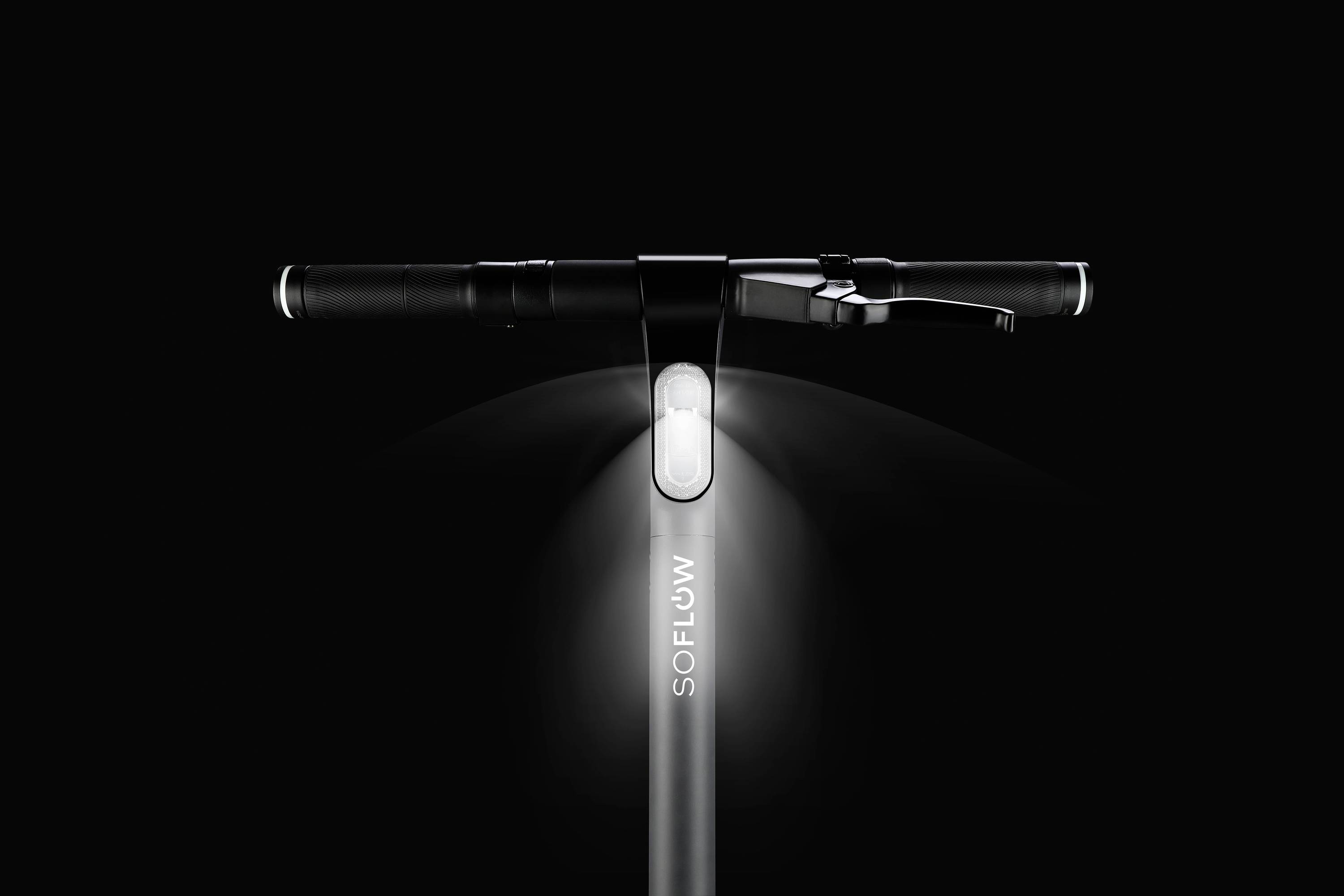 Ein schwarzer E-Scooter-Lenker mit leuchtendem Vorderlicht und der Aufschrift 'SOFLOW'. Der Hintergrund ist dunkel.