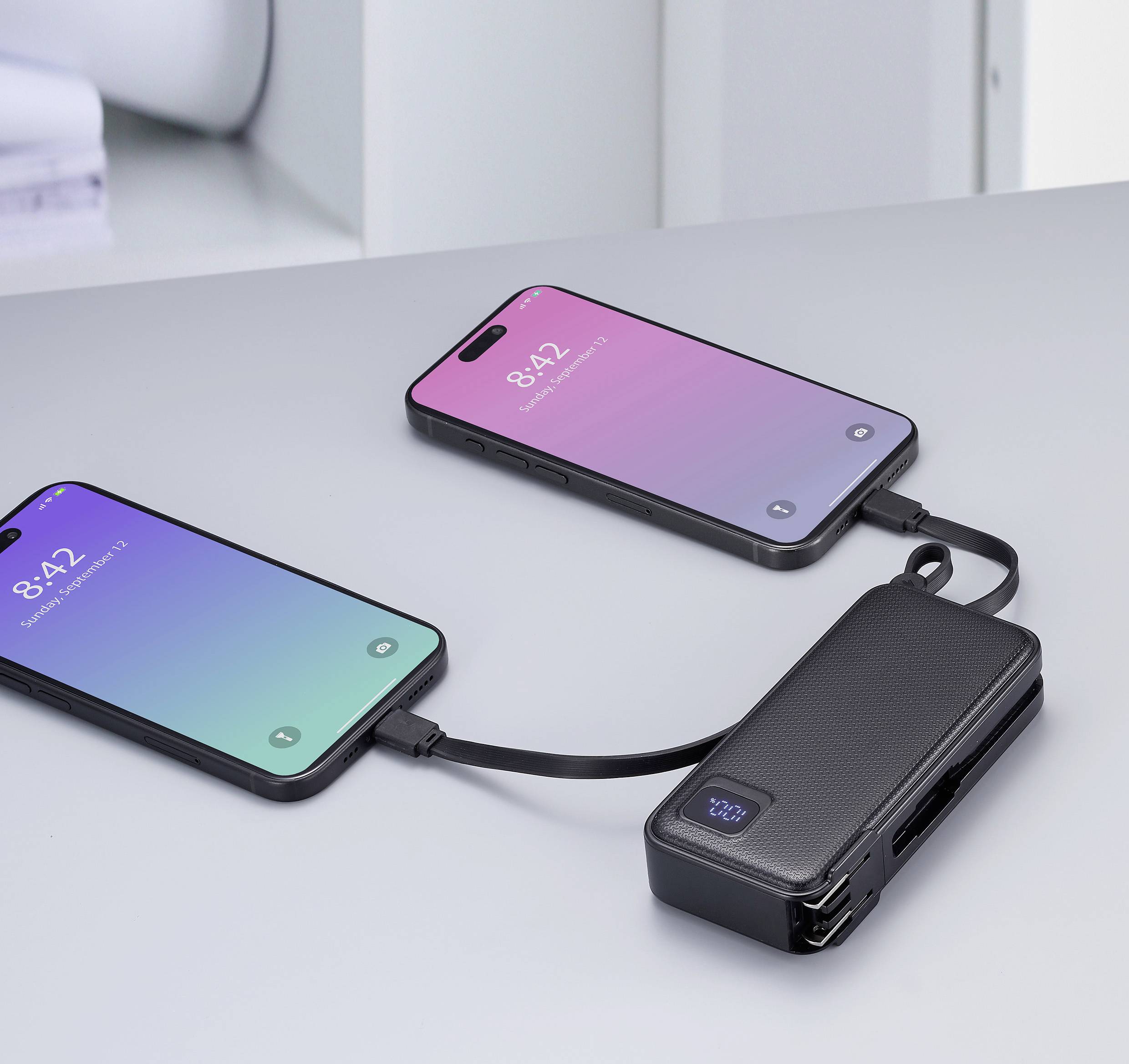 Zwei Smartphones, beide mit einem schwarzen Ladekabel an ein schwarzes Akkupack angeschlossen, laden auf einem grauen Tisch.