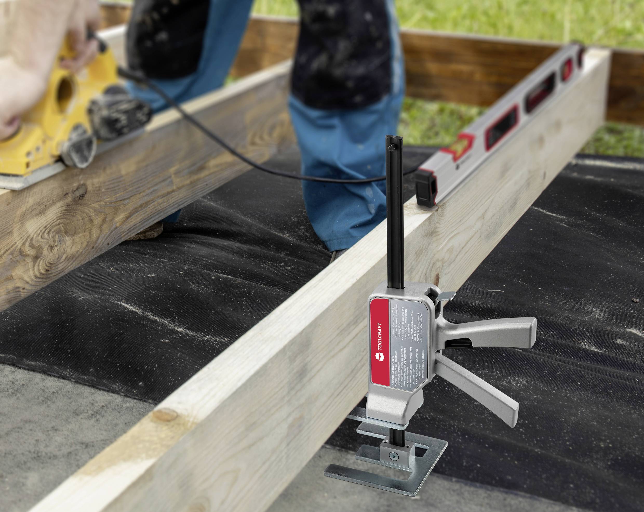 Eine Person verwendet ein Elektrowerkzeug zum Schleifen von Holz. Ein anderes Werkzeug hält zwei Balken zusammen. Eine Wasserwaage liegt auf dem Holz.
