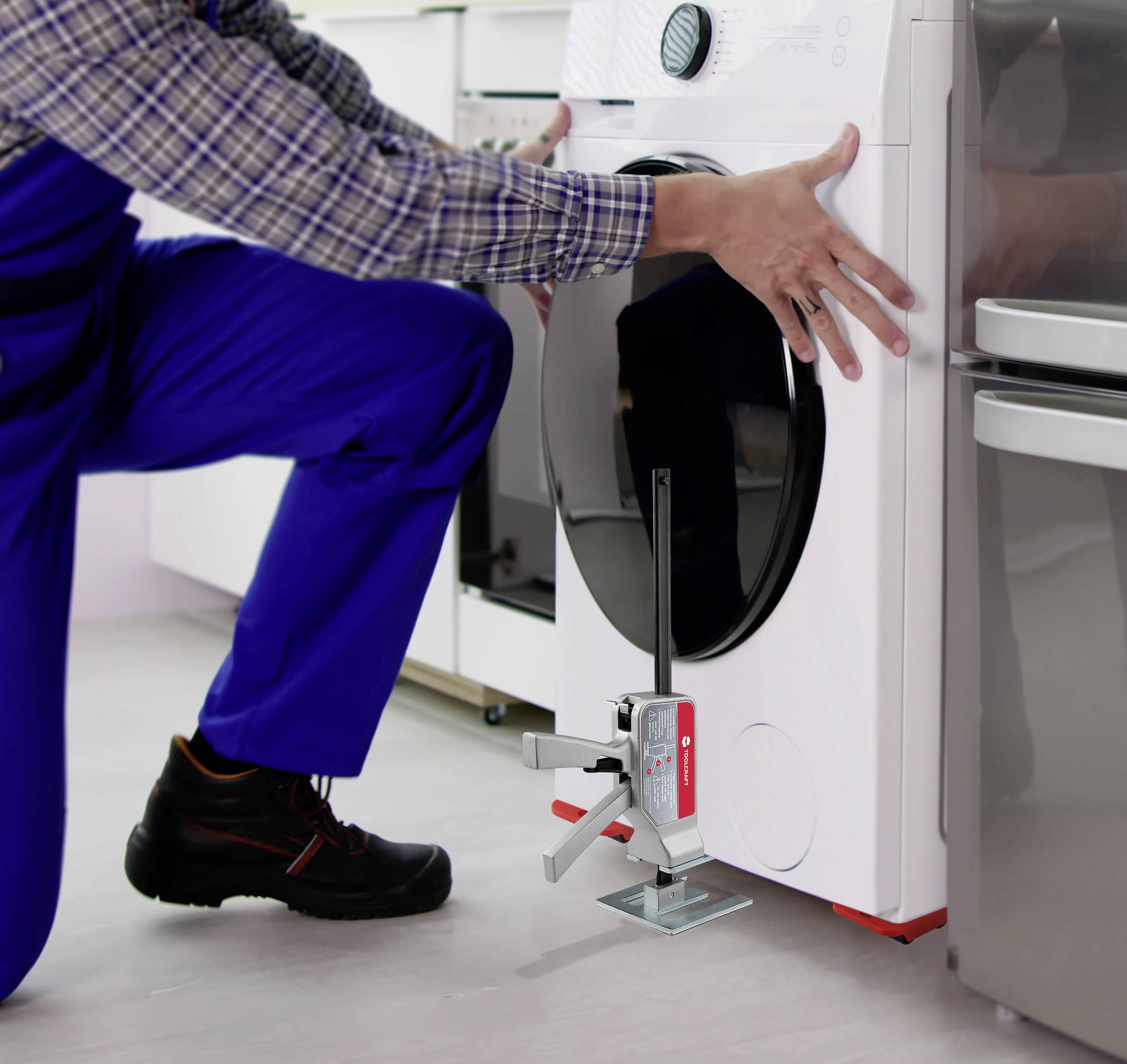Eine Person in blauer Arbeitskleidung nivelliert eine Waschmaschine mit einem Aufstellwerkzeug in einem modernen Hauswirtschaftsraum.