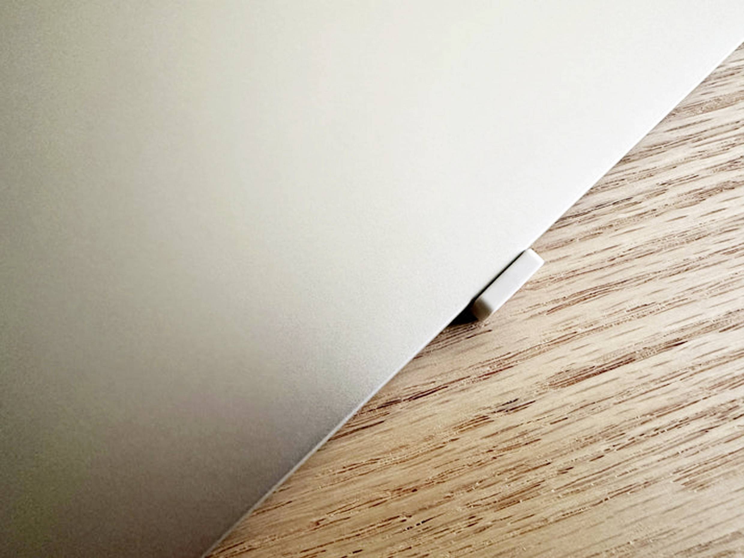 Ein Laptop, teilweise geschlossen, liegt auf einem Holztisch. Ein Teil der Ecke ragt hervor, ohne weitere sichtbare Objekte.